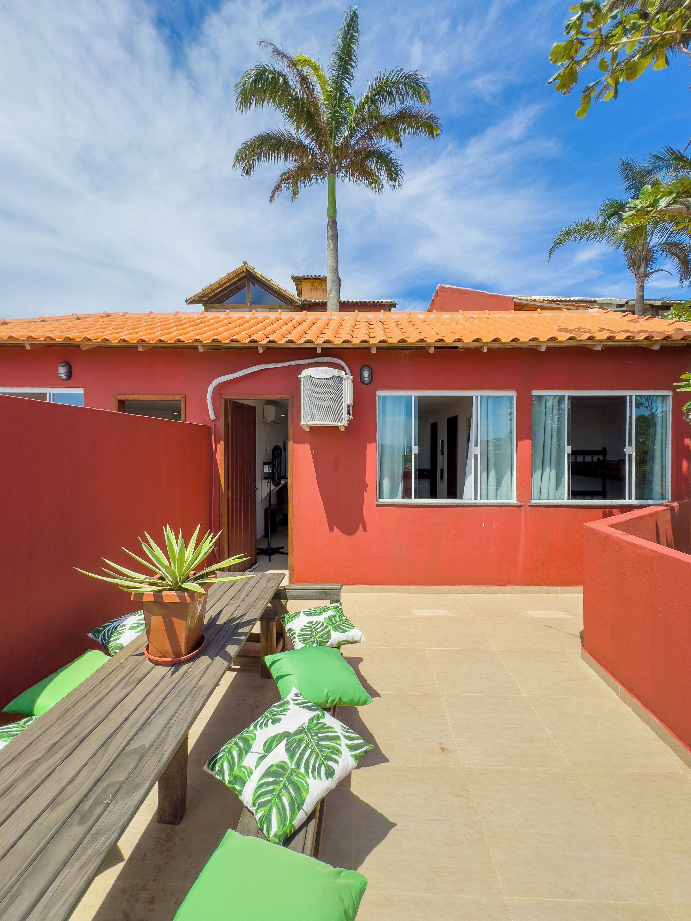 A red building with a tiled roof, a wooden bench with green cushions, and a potted plant.