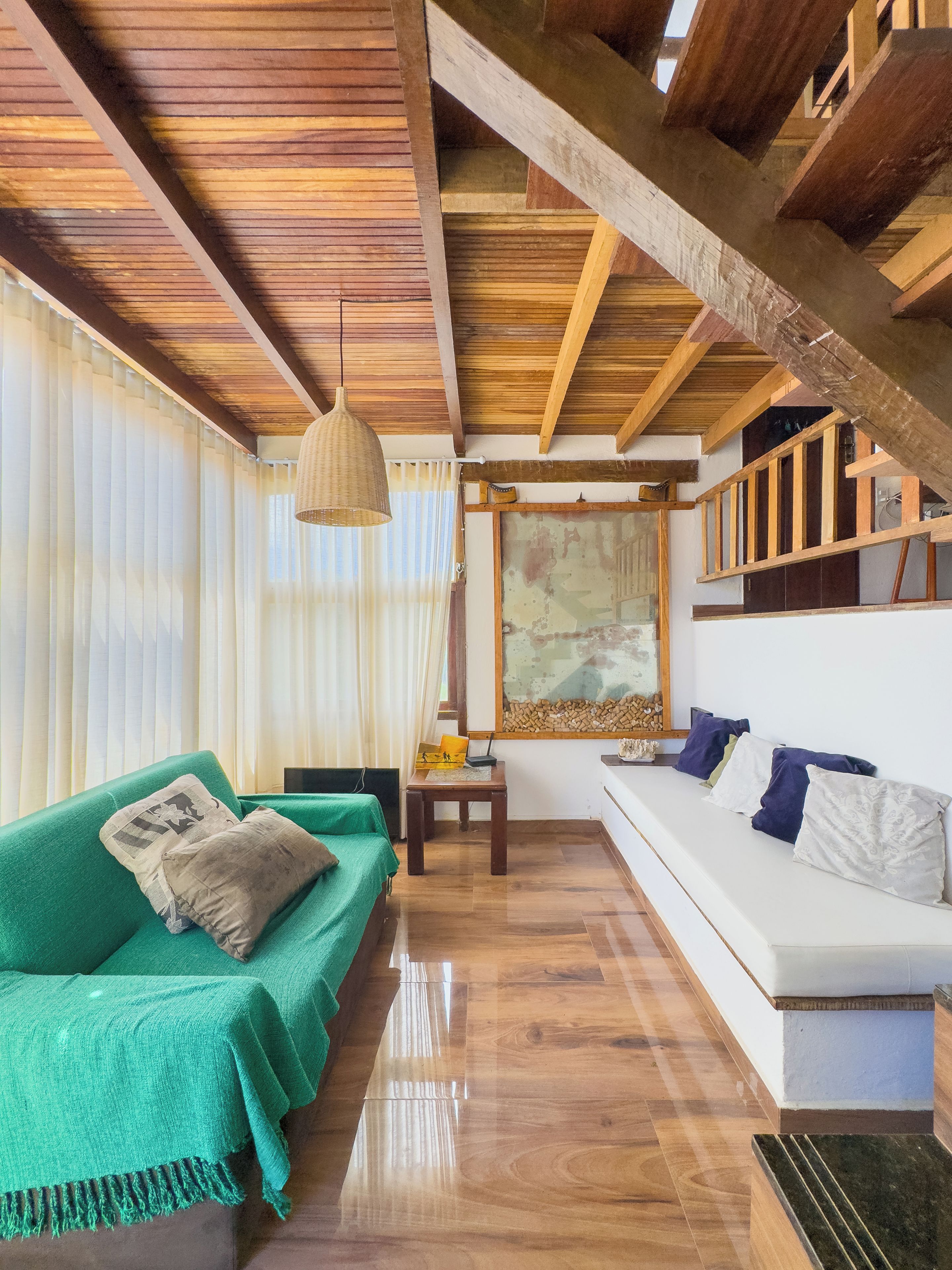 A room with a green sofa, a white couch, wooden beams on the ceiling, and a large window with sheer curtains.
