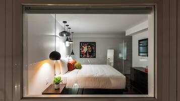 Quarto moderno com uma cama grande, abajures, uma mesinha com uma planta e um quadro na parede.