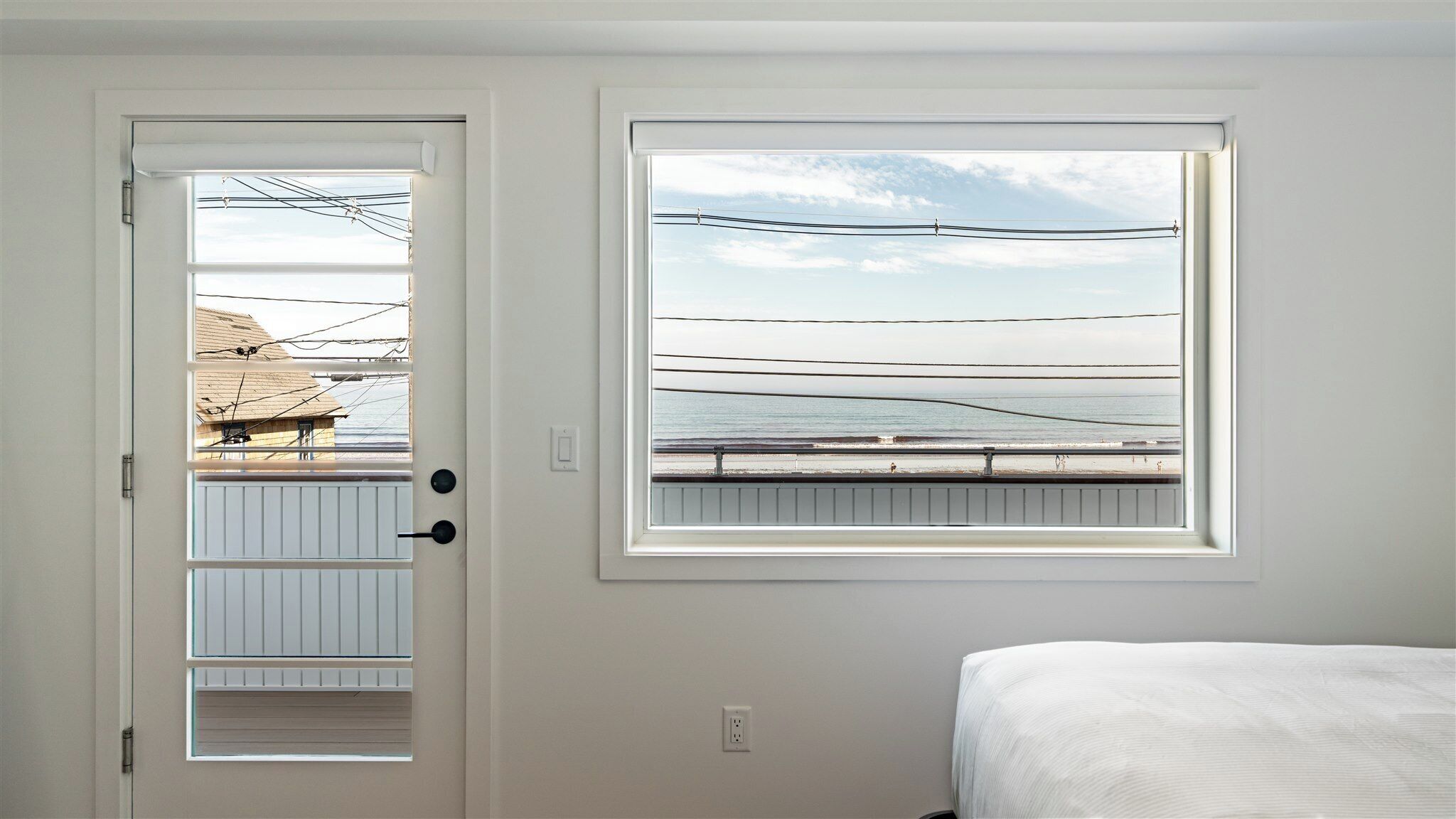 Une chambre avec un lit, une porte donnant sur une plage et une fenêtre avec vue sur un pont.