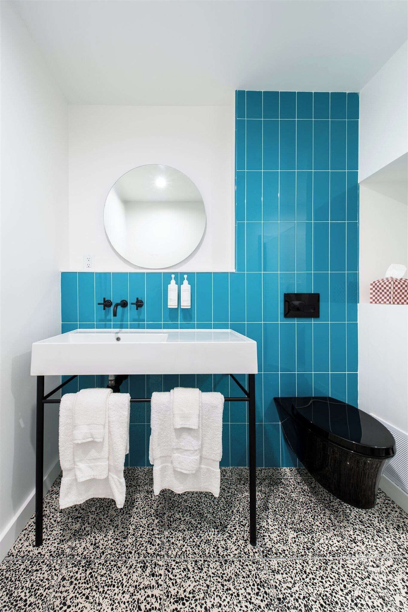 A bathroom with a white sink, blue tiles, a black bathtub, and two white towels.