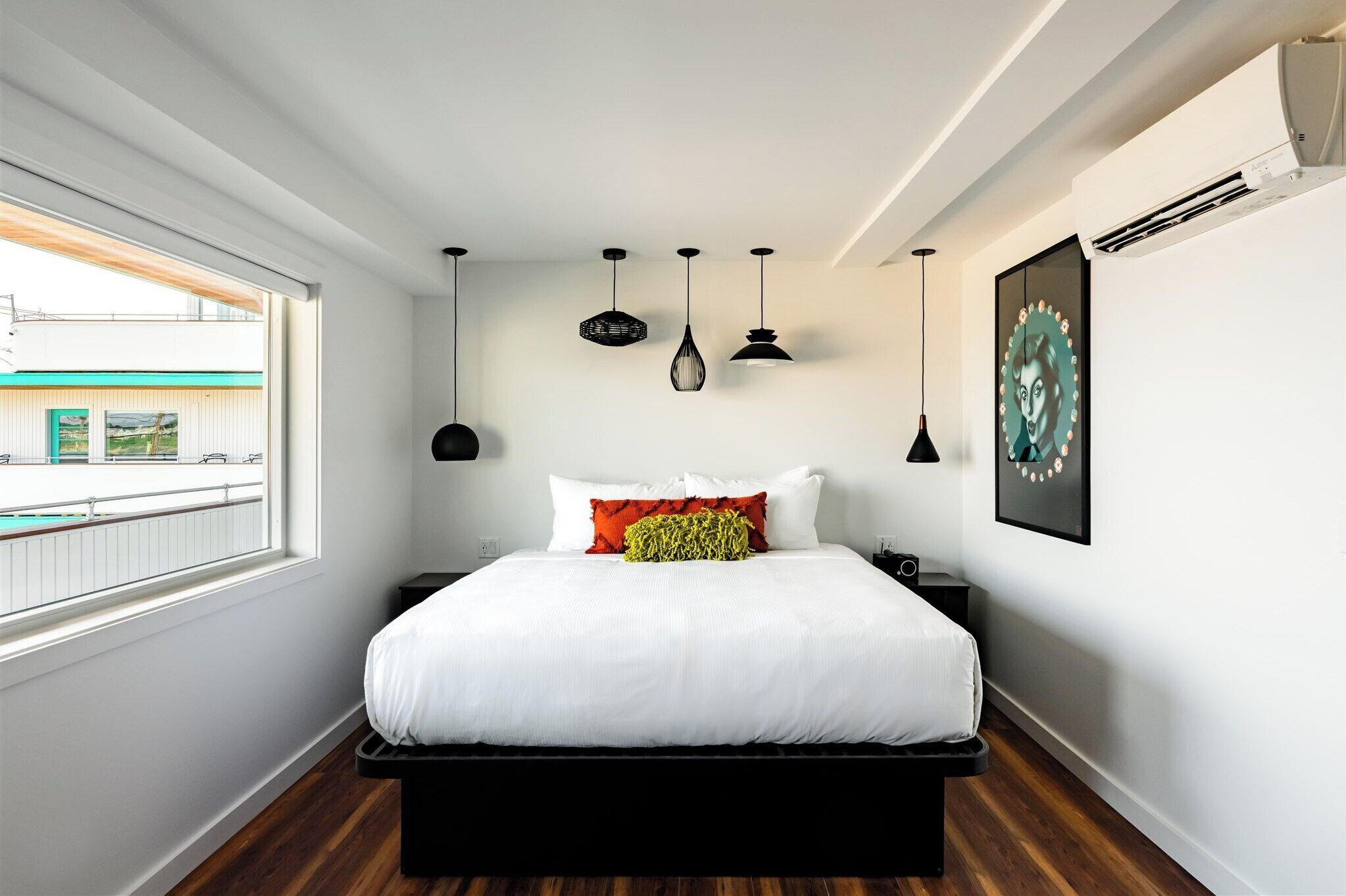 A modern bedroom with a large bed, a window with a view, and multiple hanging lights.