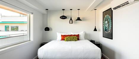 A modern bedroom with a large bed, a window with a view, and multiple hanging lights.