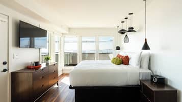 A modern bedroom with a large bed, a TV mounted on the wall, and a balcony with a railing.