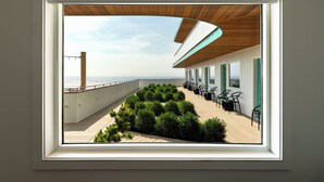 A modern rooftop terrace with a wooden deck, green hedges, and outdoor seating. - The Nevada (York Beach)