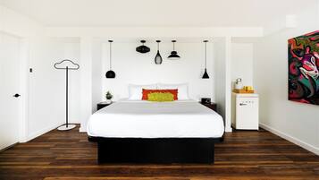 A modern bedroom with a large bed, a bedside table, a floor lamp, and a colorful abstract painting on the wall.