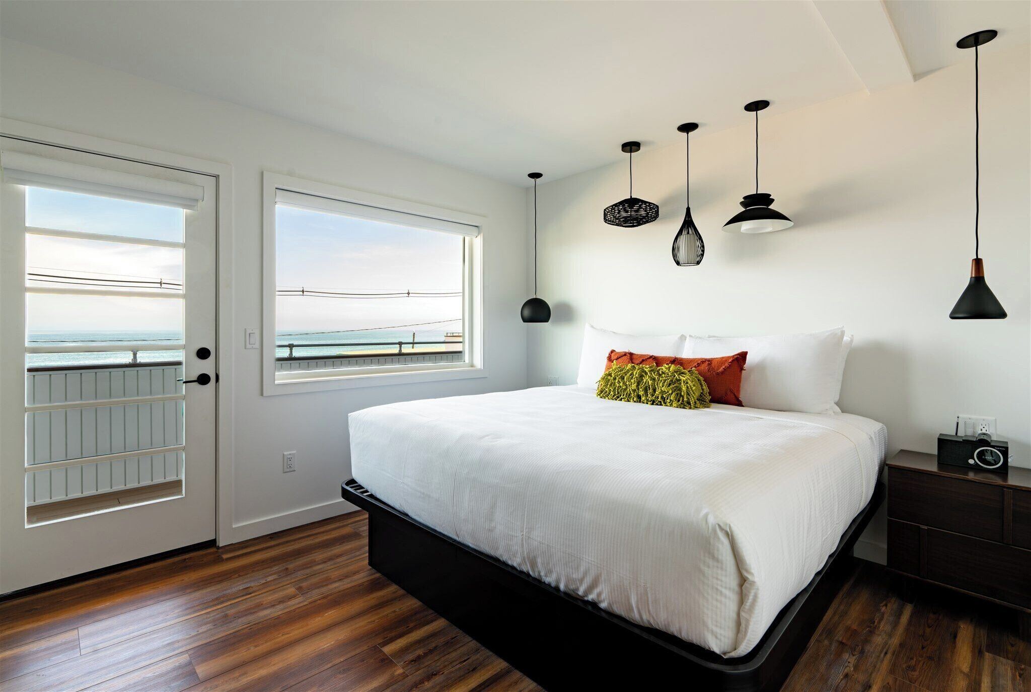 A bedroom with a large bed, a nightstand, and a view of the sea through a window.