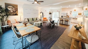 A spacious living area with a dining table, chairs, a sofa, and a kitchen area with a bar.