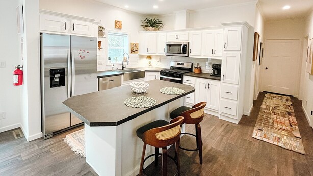 A modern kitchen with white cabinets, stainless steel appliances, a central island with stools, and a patterned rug.