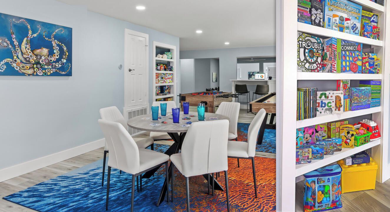 A room with a dining table, chairs, a bookshelf, and a colorful rug.