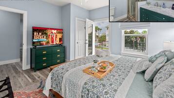 A modern bedroom with a TV, a green dresser, a bed with a floral bedspread, and a view of the outdoors.