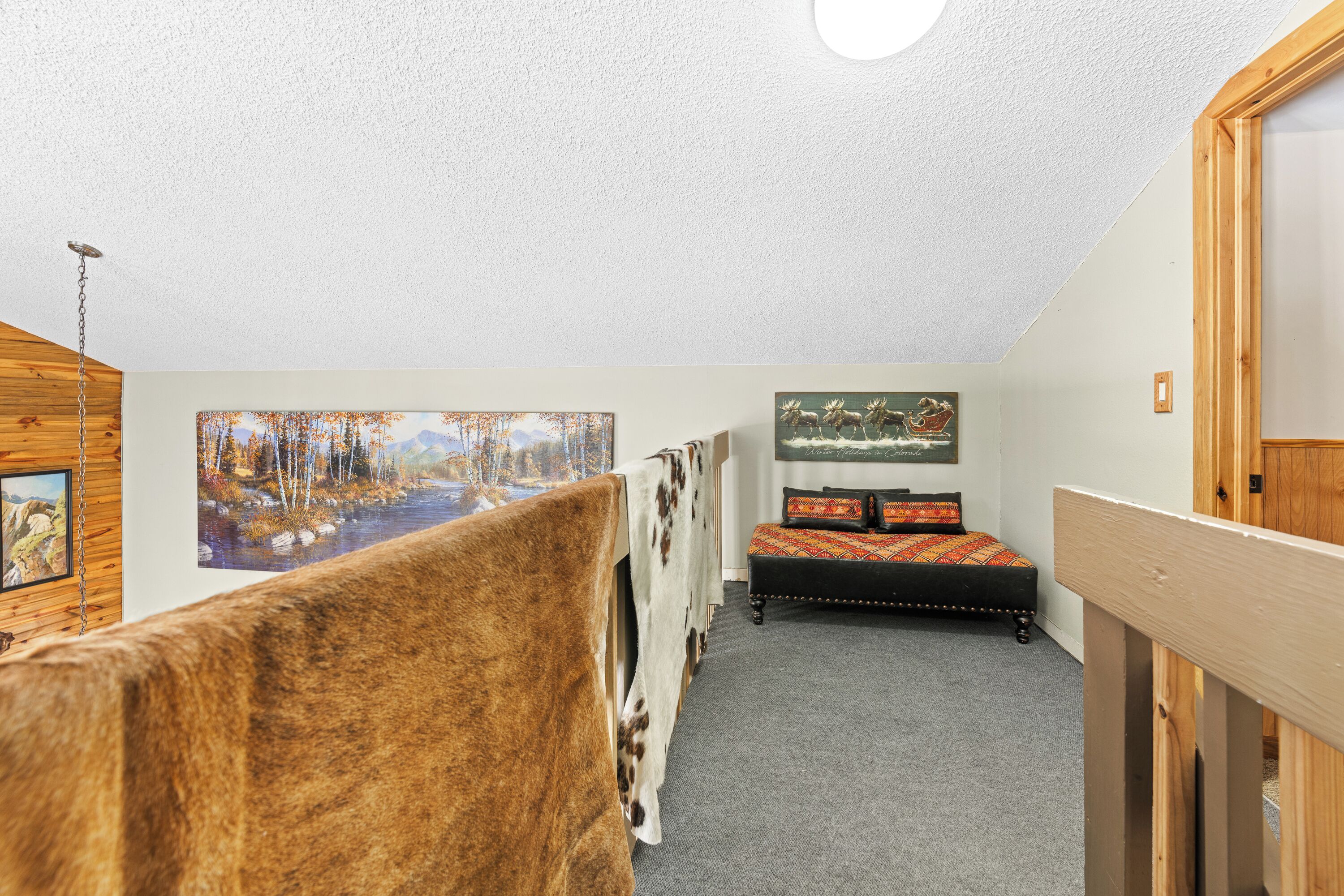 A bedroom with a cowhide headboard, a bed with a colorful blanket, and a painting of a forest scene on the wall.