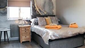 Un dormitorio con cama, mesita de noche, lámpara, radiador y una ventana.