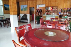 En matplats med ett runt bord i glas och röda stolar, en bokhylla i trä och en öppen spis.