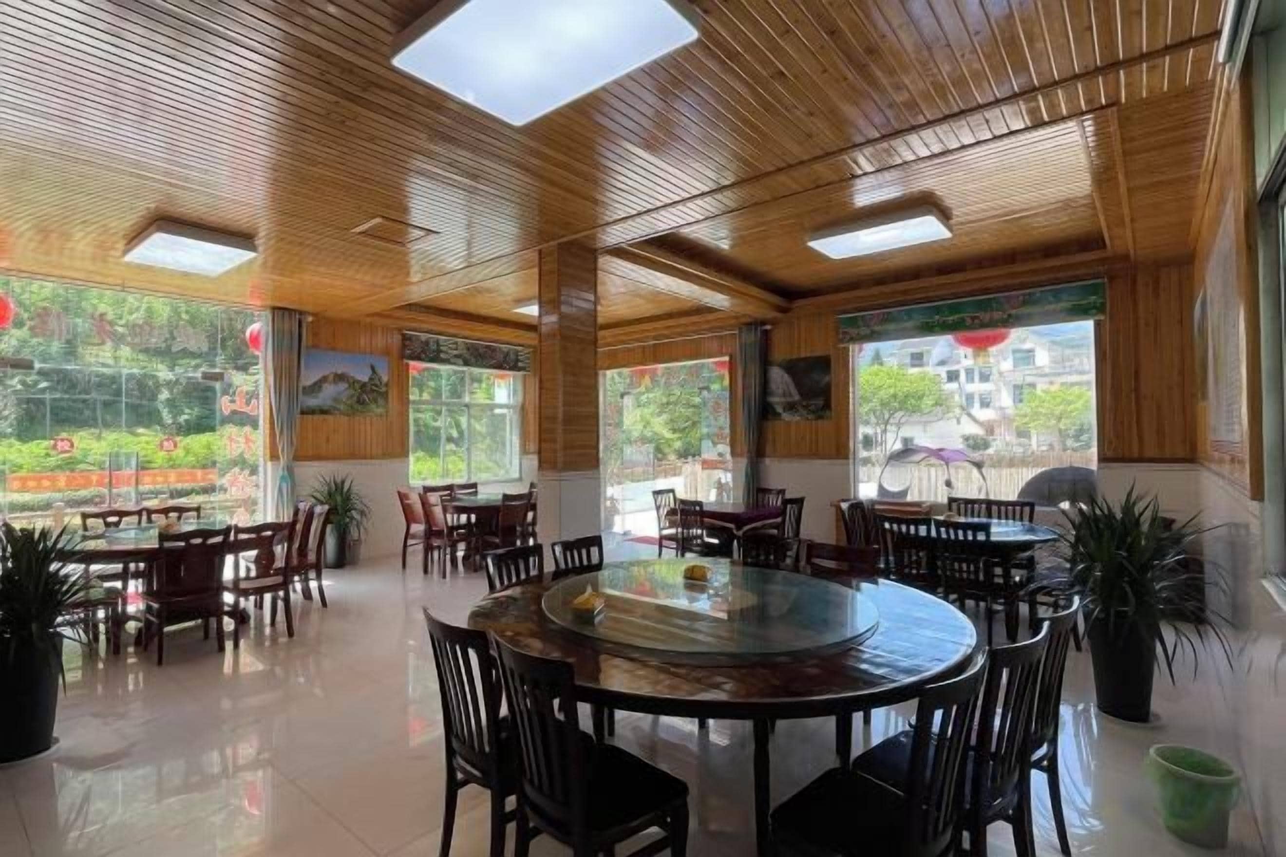 A spacious indoor area with multiple round tables and chairs, large windows, and a wooden ceiling.