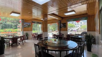 A spacious indoor area with multiple round tables and chairs, large windows, and a wooden ceiling.