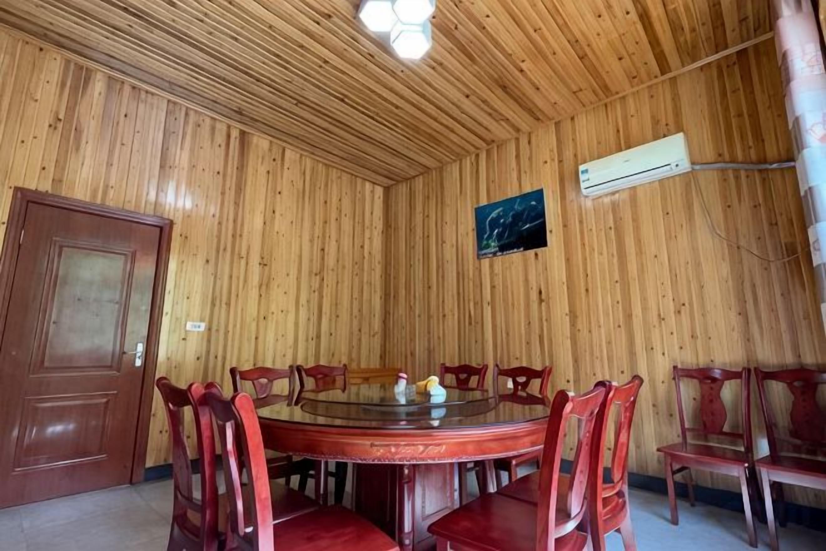 A wooden-paneled room with a round table and chairs, an air conditioning unit, and a door.