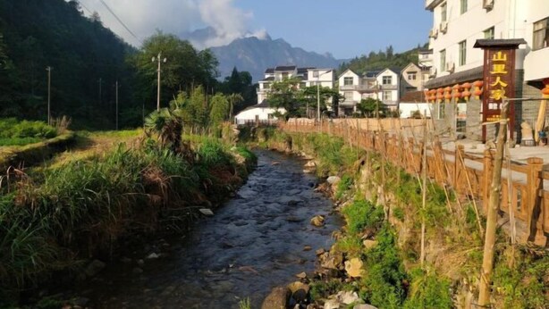 Ein Fluss fließt durch ein Wohngebiet mit Häusern an einer Seite und einem Berg im Hintergrund.