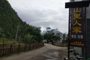 L’entrée d’un hôtel, avec un panneau indicateur, un chemin pavé et une chaîne de montagnes en arrière-plan.