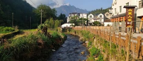 A river flowing through a residential area with houses on one side and a mountain in the background.