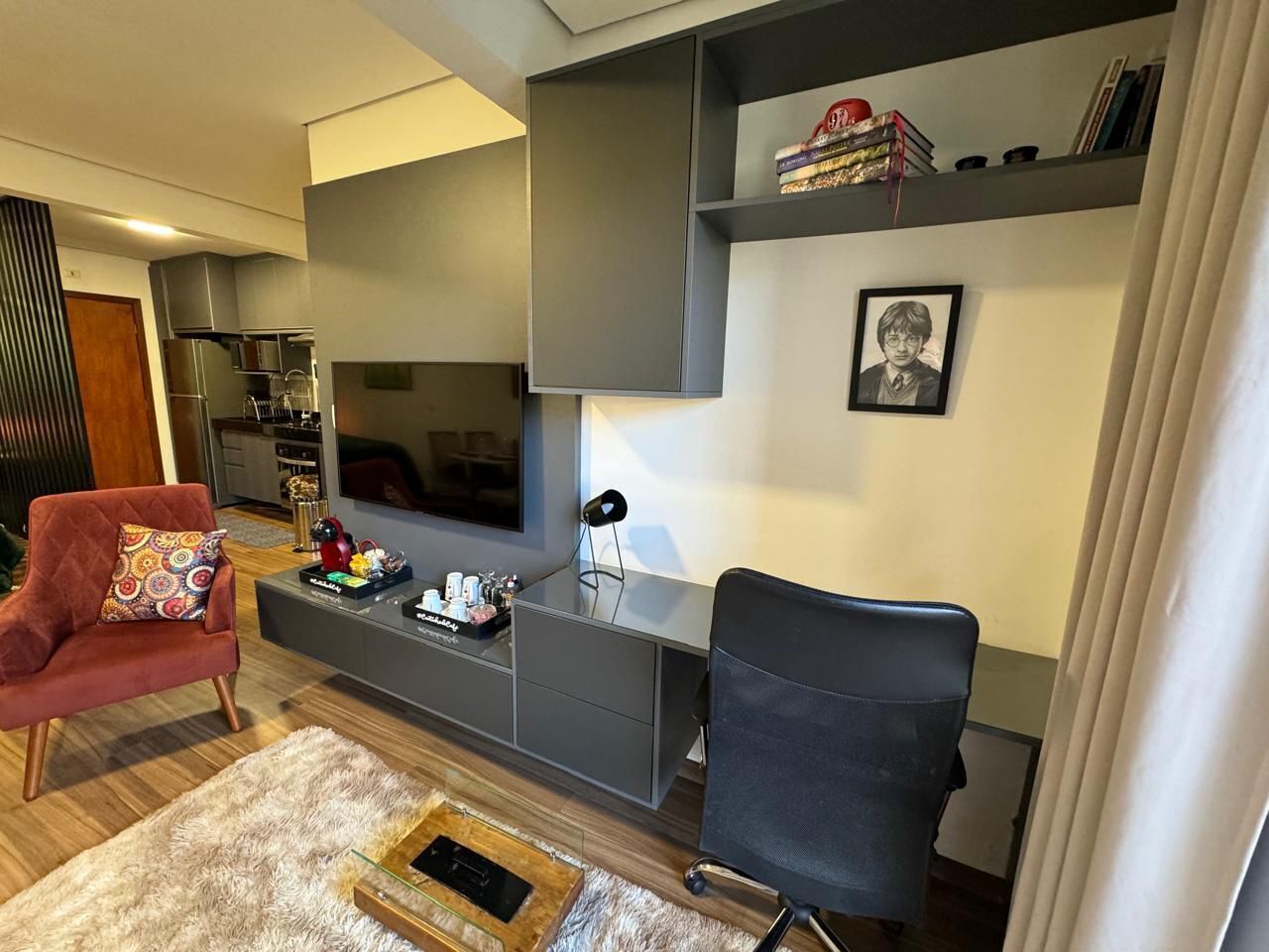 Un salon moderne avec un meuble de rangement gris pour l’équipement audiovisuel, un téléviseur à écran plat, un fauteuil rouge, une chaise de bureau noire et une petite bibliothèque contenant des livres et des objets décoratifs.