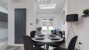 A modern dining area with a glass table set for four, black chairs, a black floor lamp, and a view of the outdoors through a glass door.