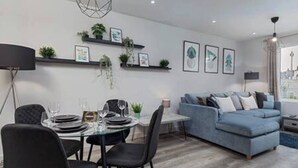 A modern living room with a blue sofa, a dining table set for four, and a small kitchen area.