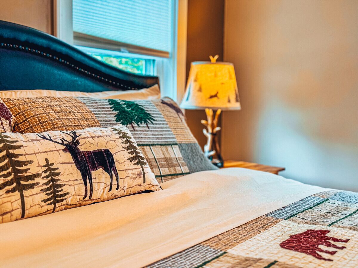 A neatly made bed with patterned pillows, a bedside lamp, and a window with blinds.