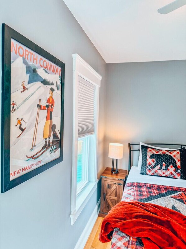 Un dormitorio con cama, mesita de noche, lámpara, ventana con persianas y un cartel en la pared.