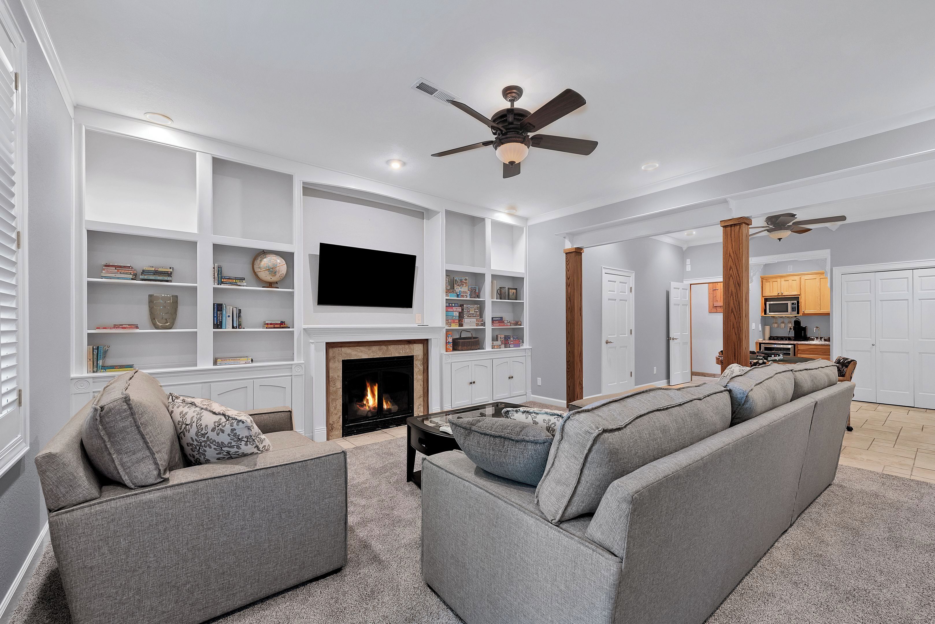A spacious living room with a fireplace, built-in shelves, a large flat-screen TV, and a ceiling fan.