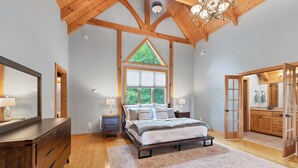 A bedroom with a large bed, wooden ceiling beams, a window, and a view of greenery outside. - This Amazing home has much to offer ,spacious rooms & and a hot-tub for relaxing (Townsend)