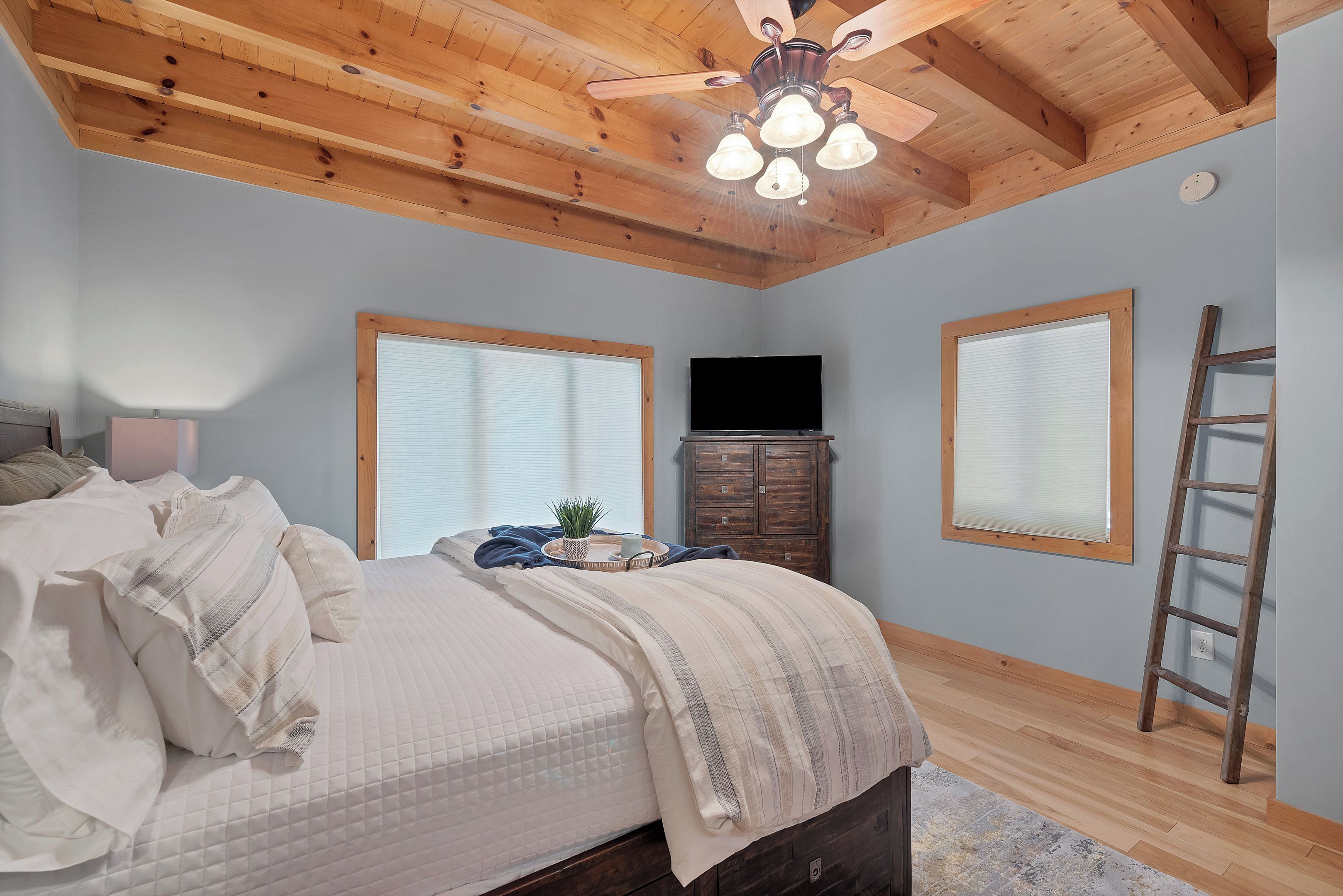 A bedroom with a bed, a ceiling fan, a TV, and a window.