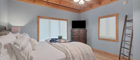 A bedroom with a bed, a ceiling fan, a TV, and a window.