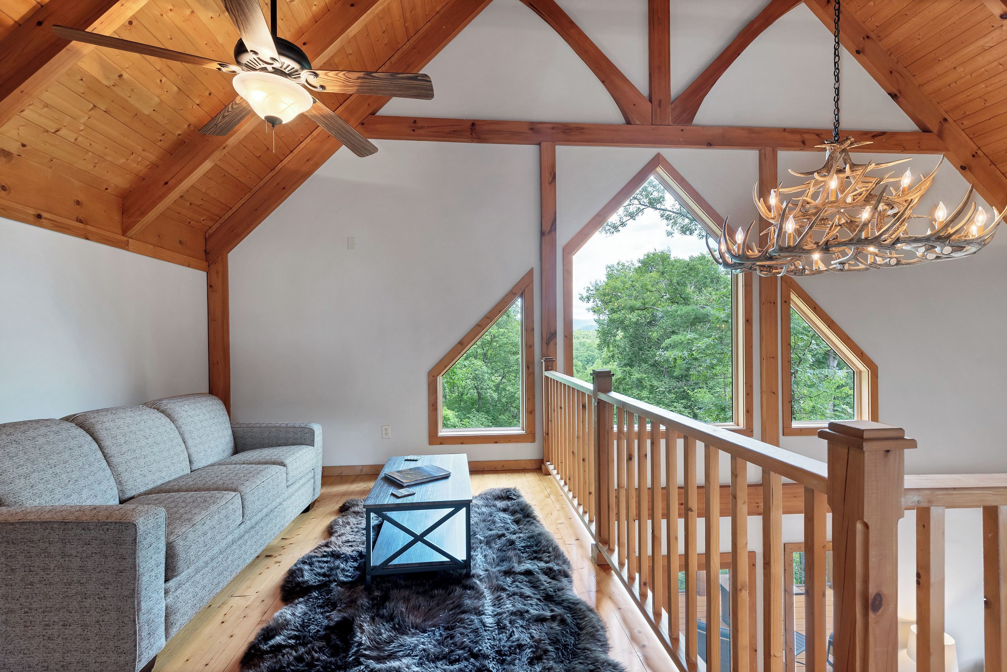 A loft-style room with a wooden ceiling, a gray sofa, a fur rug, and a chandelier.