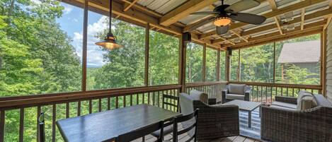 A covered outdoor deck with a table and chairs, a sofa, and a ceiling fan.
