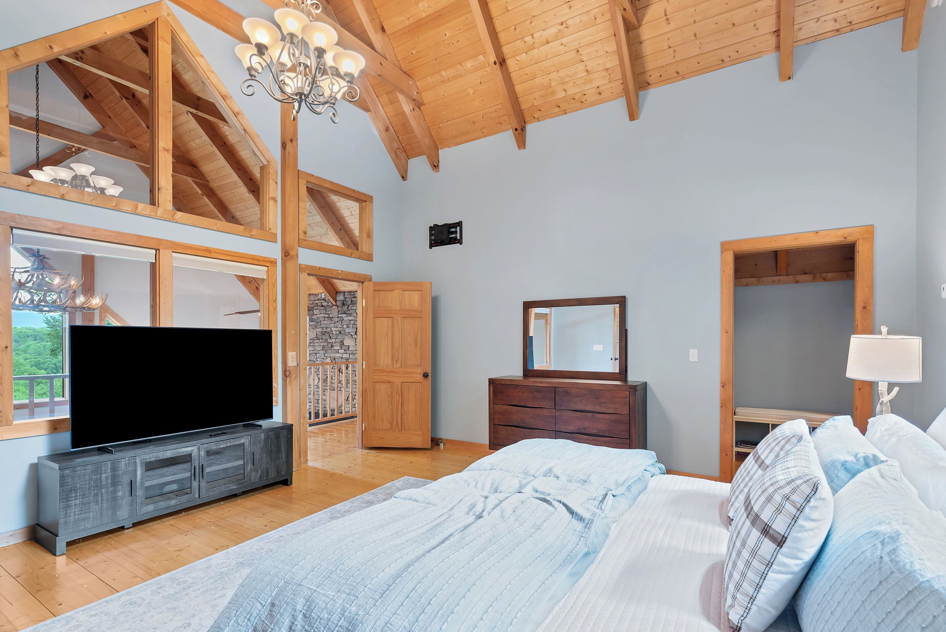 Un dormitorio amplio con una cama grande, un televisor sobre un mueble de madera, un aparador y un espejo.