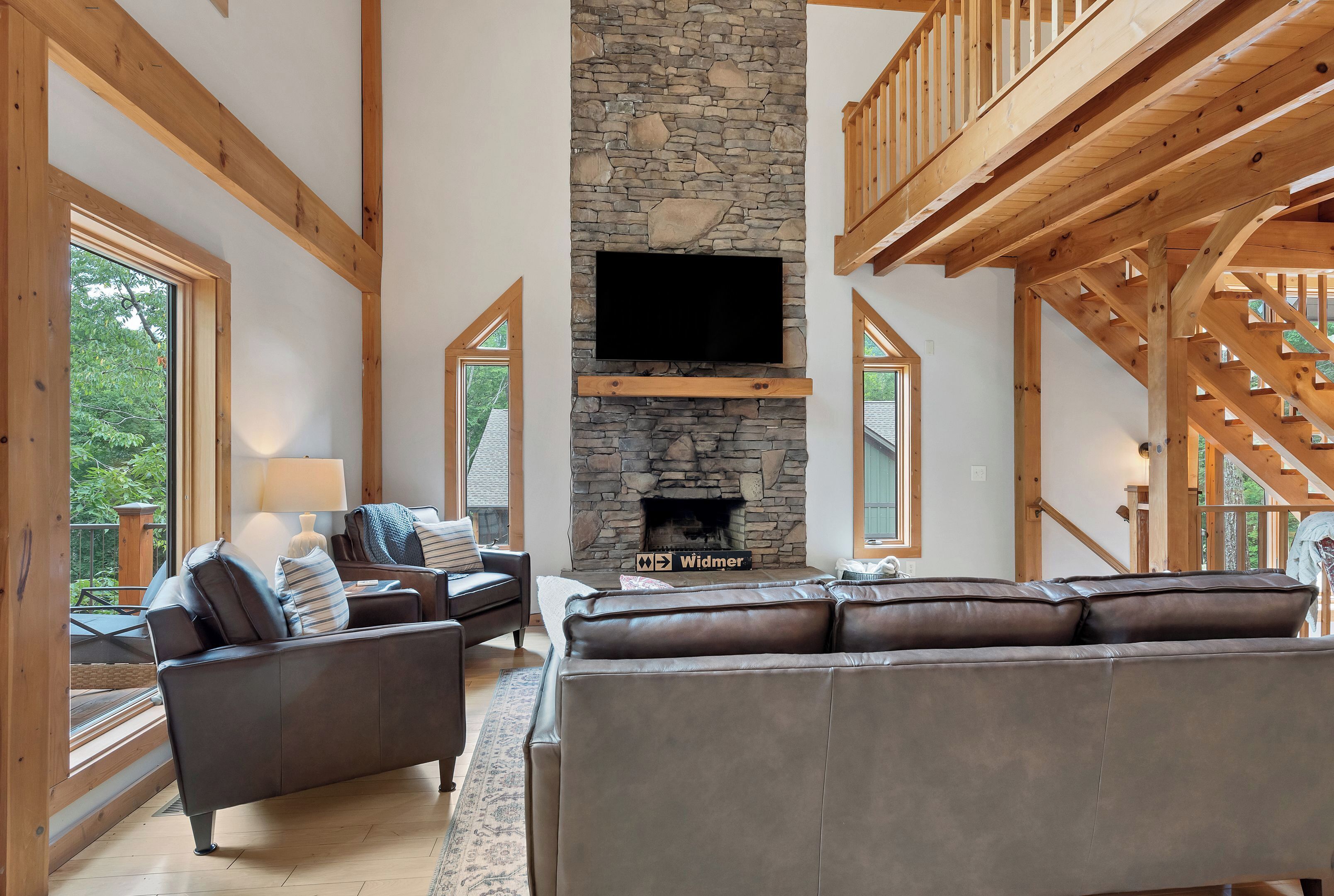 A spacious living room with a stone fireplace, wooden beams, and a large flat-screen TV.