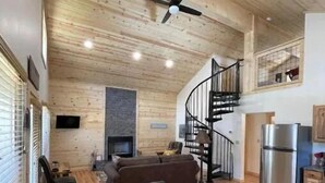 A spacious living area with a high ceiling, wooden walls, a fireplace, a dining table with chairs, and a kitchen area with a refrigerator and stove. - 4K River Ranch • River Cabin 2 (sleeps 6) (Red River)