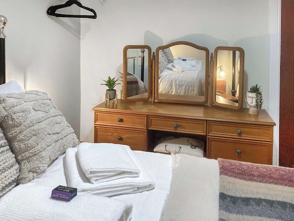 A neatly made bed with white towels, a wooden dresser with mirrors, and a small plant on the dresser.