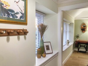 Un passadís amb una banca de fusta, un vas amb flors seques i un quadre encimbellat a la paret.
