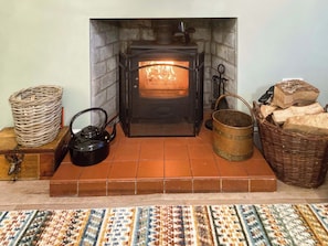 A fireplace with a fire, surrounded by a woven basket, a kettle, a bucket, and a wicker basket filled with wood.