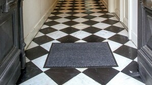 Un pasillo con piso a cuadros blanco y negro, un felpudo y una escalera que lleva a otra habitación.