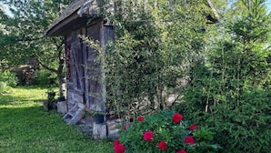 A rustic wooden structure with a sloped roof, surrounded by lush greenery and red flowers. - One Bedroom Apartment with Balcony (Gajić)