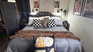 Une chambre à coucher avec un lit, un coussin à carreaux, une couverture à motifs léopard et un mur orné de tableaux encadrés.