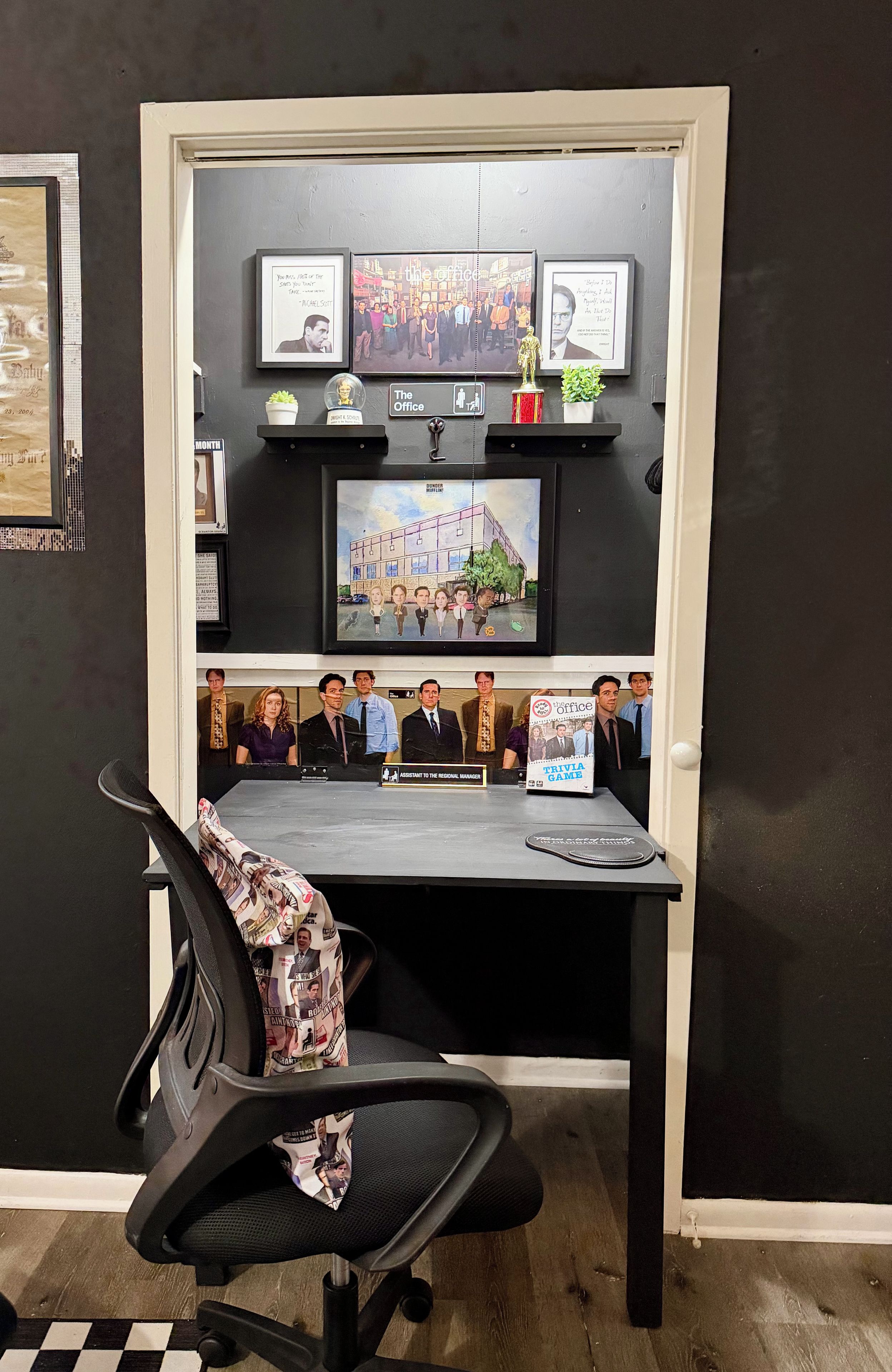 A workspace with a desk, chair, and various framed items on the wall.