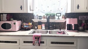A kitchen with white cabinets, a microwave, a sink, and a window with a curtain. - Woodlands Studio Stay • The Sweet Escape • (Conroe)