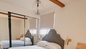 Une chambre à coucher avec un grand lit, une chaise en bois, un miroir et un luminaire suspendu.