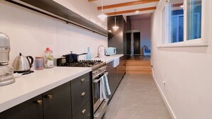 Une cuisine moderne avec des meubles de couleur sombre, un plan de travail blanc et un four encastré. Il y a une fenêtre sur le côté droit et une porte qui donne sur une autre pièce.