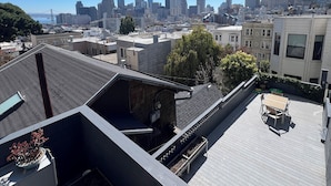 Un toit-terrasse offrant une vue sur les toits d’une ville, avec un pont en particulier, ainsi qu’un espace patio comprenant une table et des chaises.