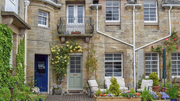 Un bâtiment en pierre avec une porte verte, un balcon doté d’une balustrade et un jardon à l’avant.